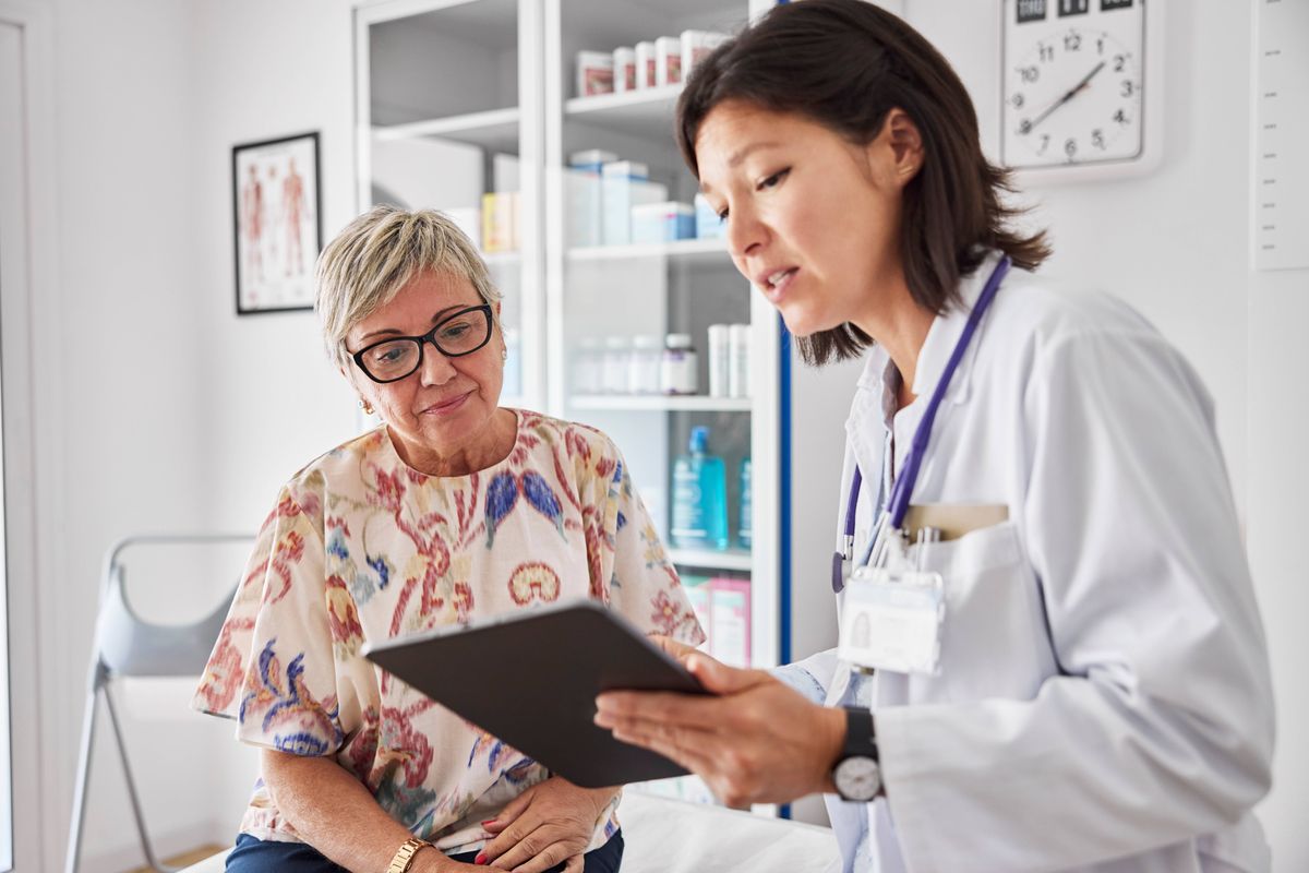 Female doctor sharing electronic test results with patient at clinic. Medical expert and woman are examining reports. They are sitting in examination room.