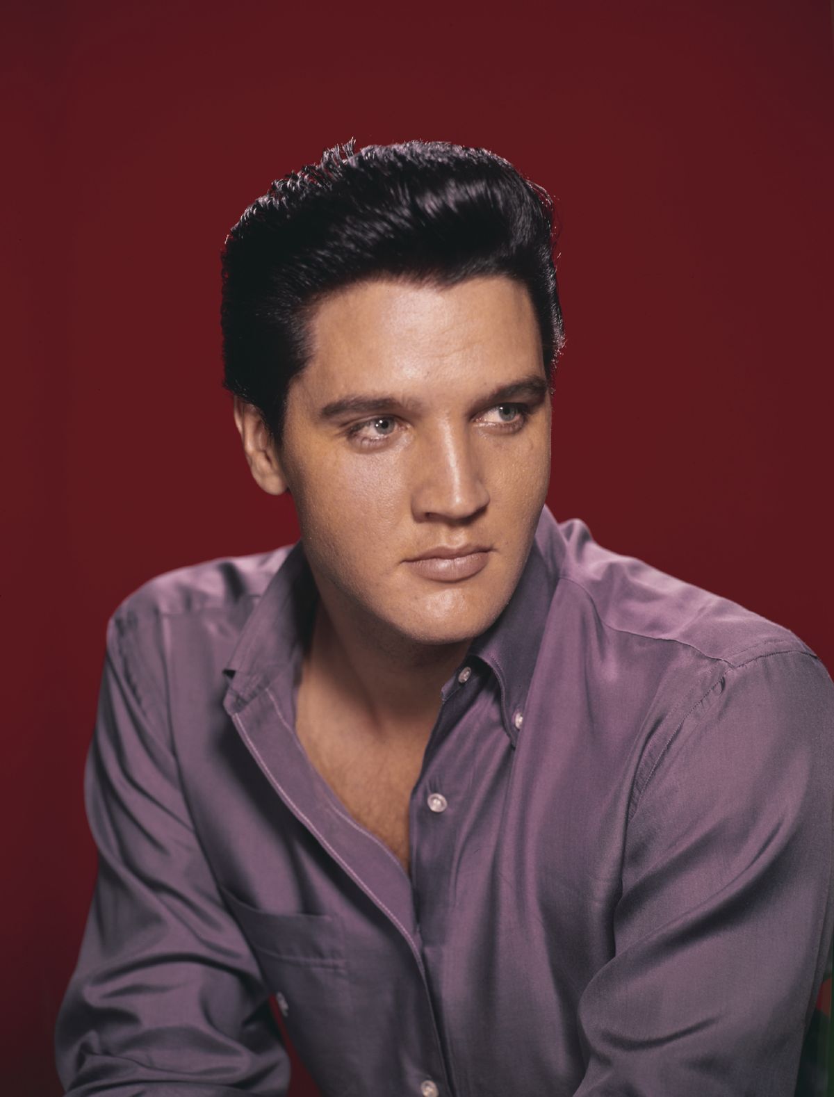 A portrait of American singer and actor Elvis Presley wearing a purple shirt circa 1956.