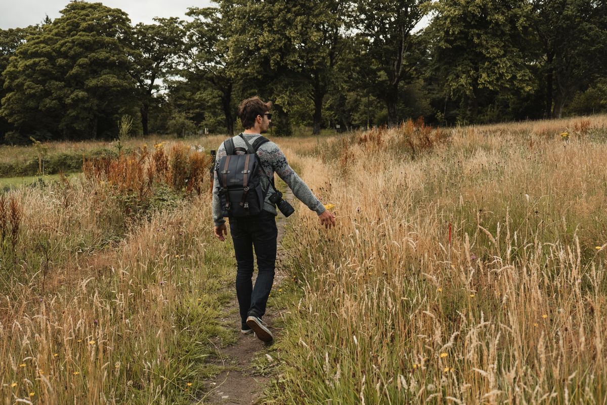 white young man walking through a meadow with blue backpack