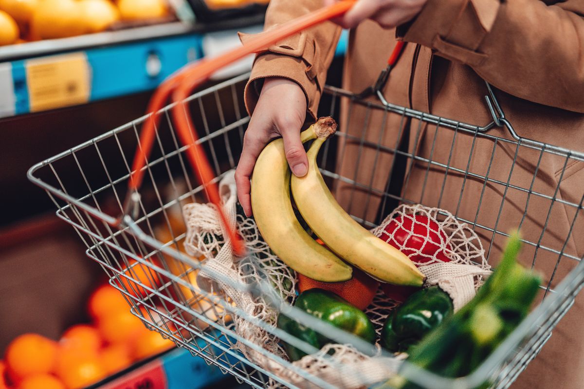 Cropped shot of female hand carrying shopping basket while choosing vegetables at supermarket. Grocery shopping concept.