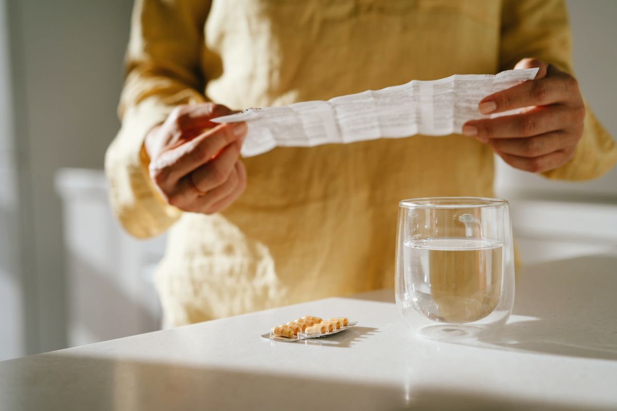 Woman takes pill with water and reads safety leaflet