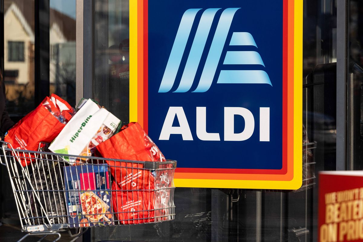 An ALDI store display with a shopping cart filled with assorted products in front of the ALDI logo and sign.