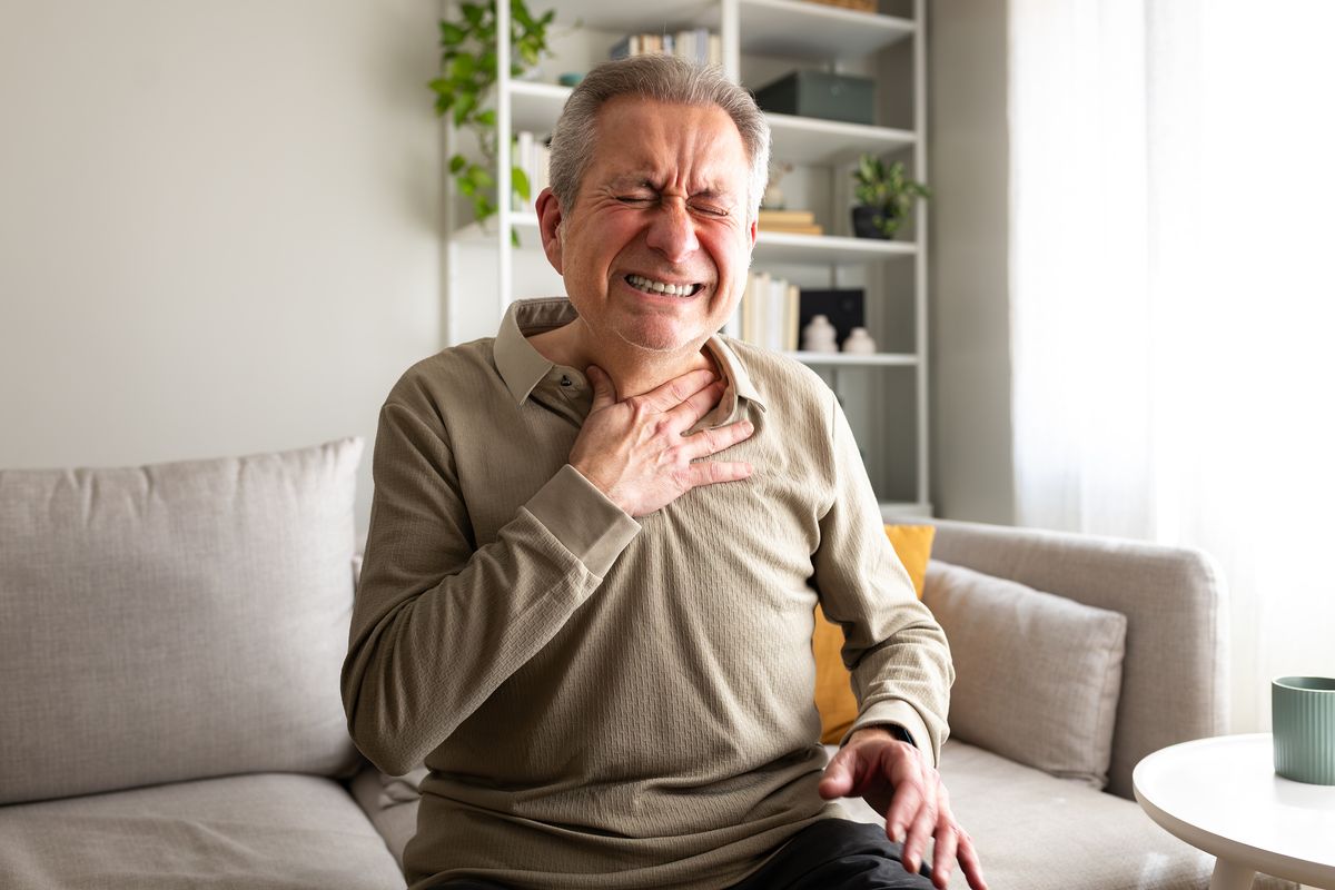 Senior man suffering from chest pain or heart attack, sitting on sofa at home