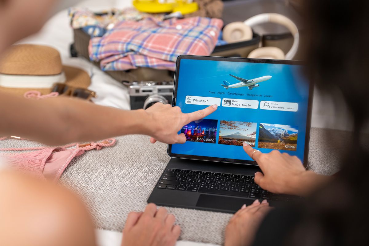 Two young adults engaged in selecting their next travel destination while using a tablet, surrounded by clothes and accessories, embodying a spirit of adventure and leisure planning