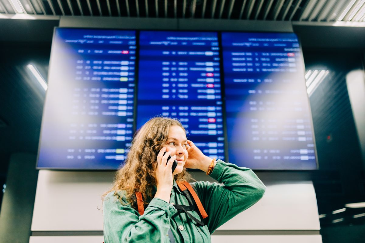 Woman calling on phone at airport departure board