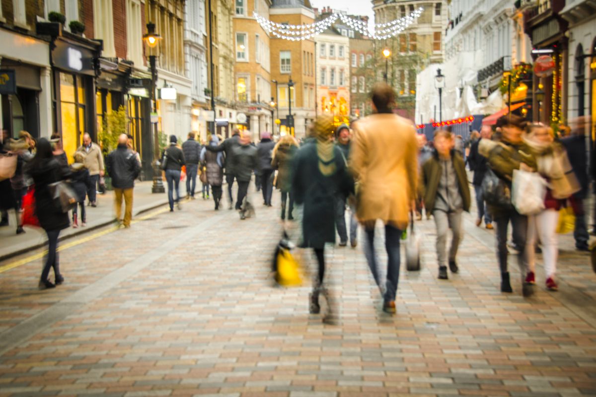 A busy high street scene with a couple holding hands and walking past fashion shops