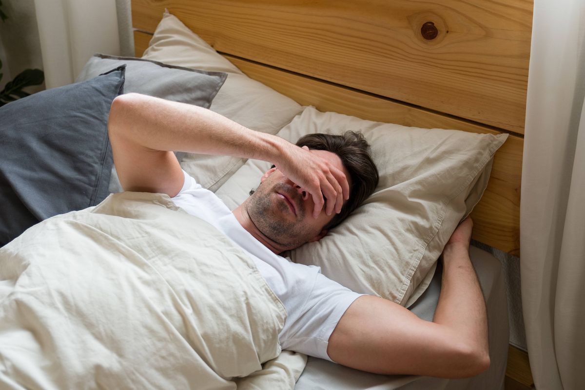 Man covering his eyes in bed, experiencing migraine, headache, or eye strain