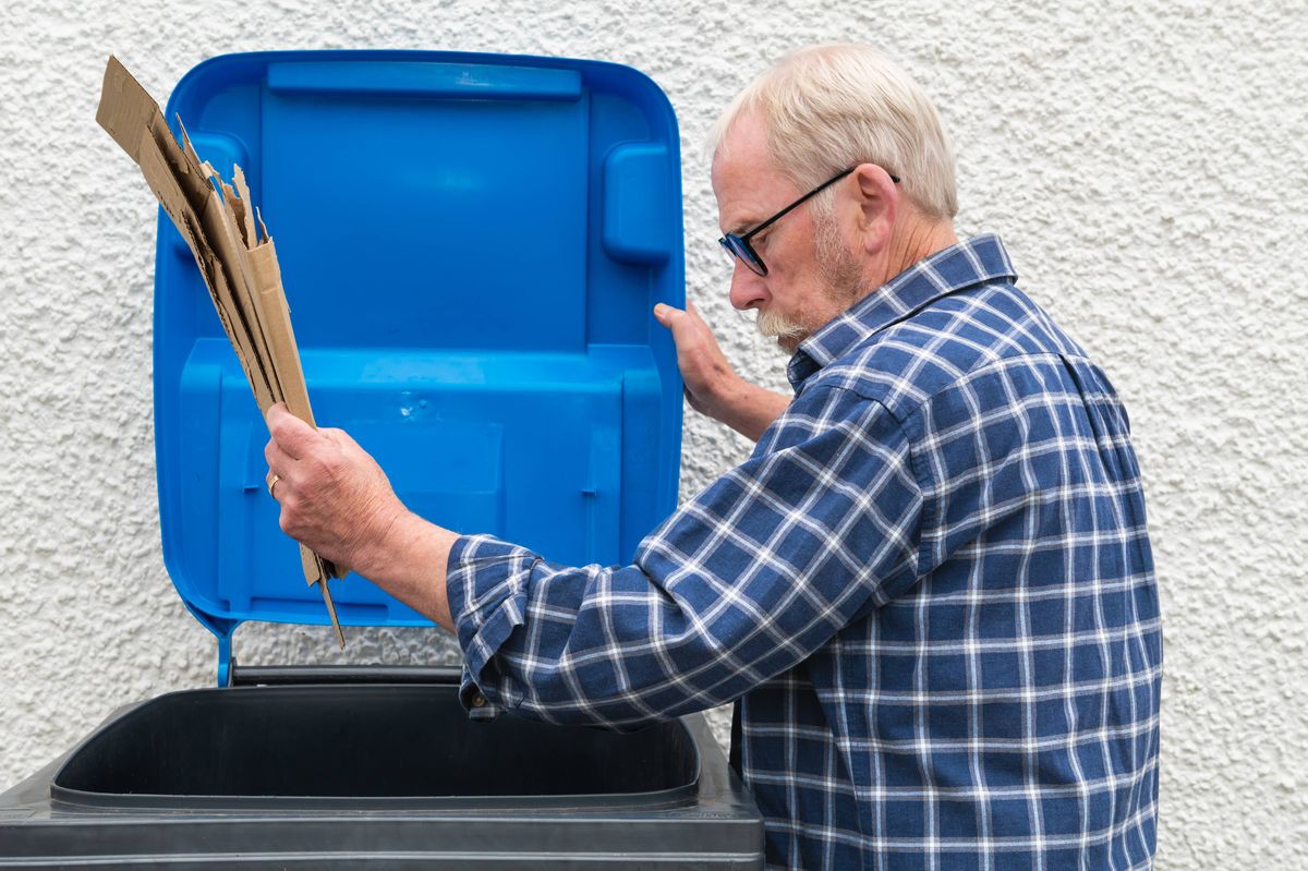 Mature man putting cardboard into a home recycling bin in his back yard in Scotland