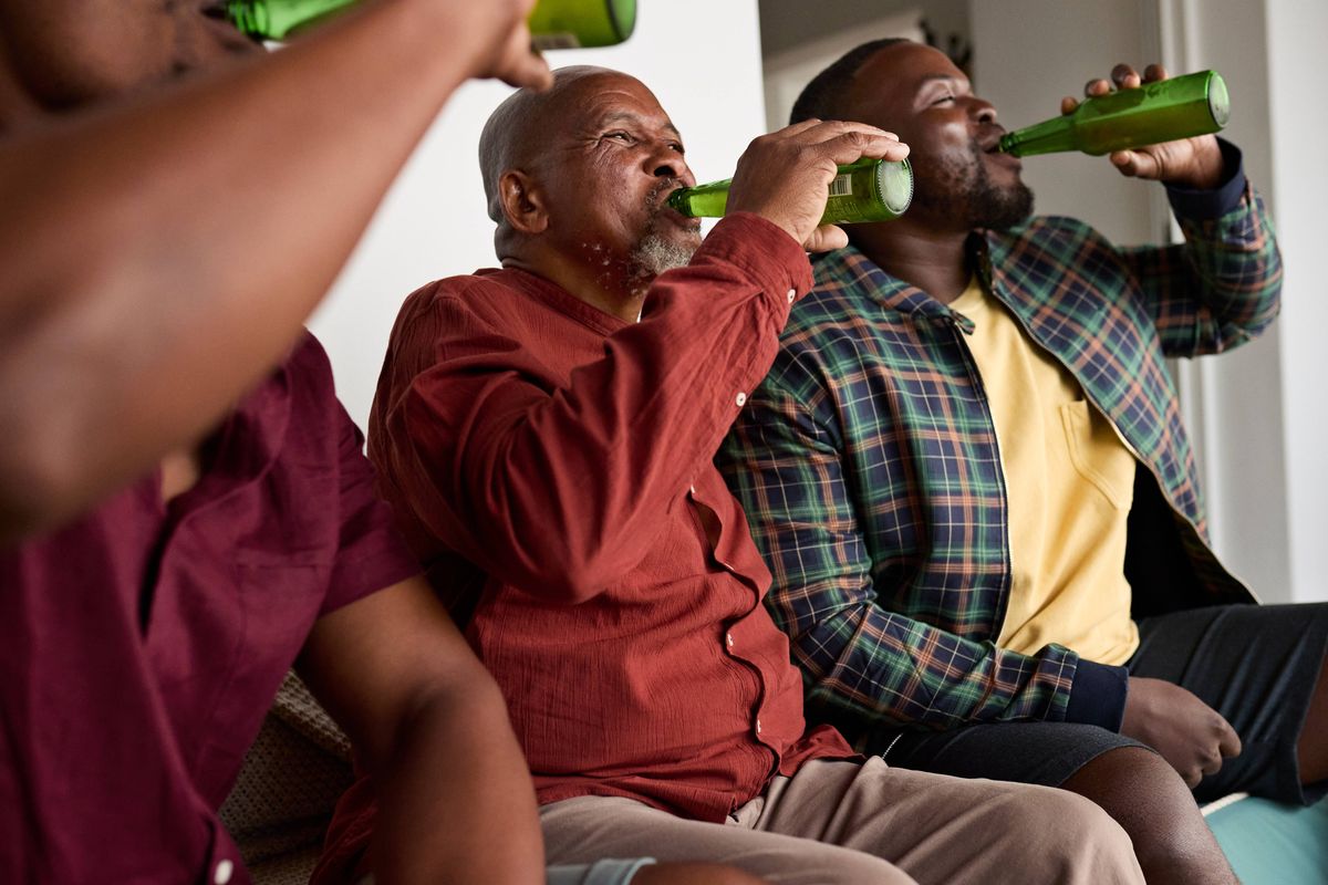Men drinking beer while sitting together on sofa at home