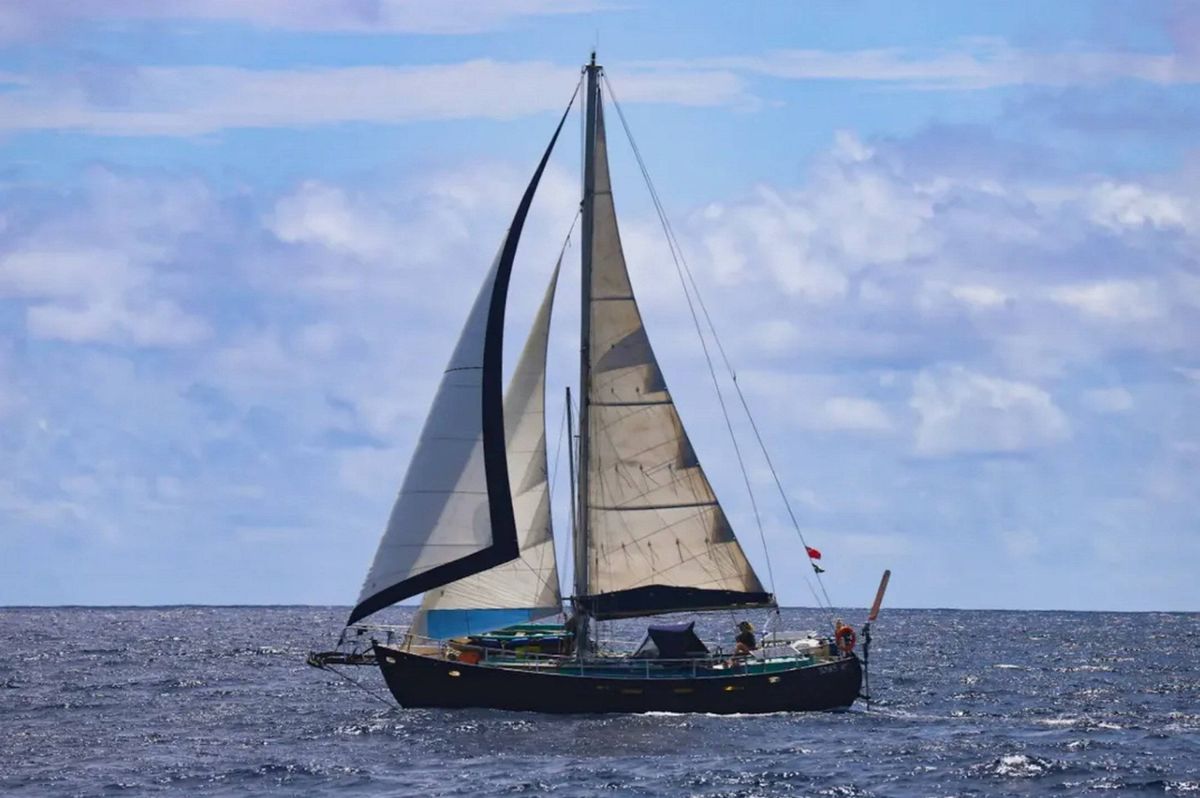 An image shows a sailboat navigating on a body of water with a cloudy sky in the background.