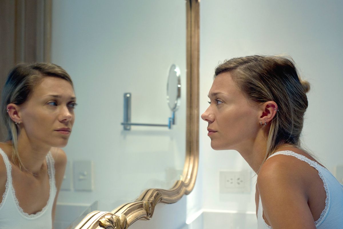 Woman looking at self in bathroom mirror
