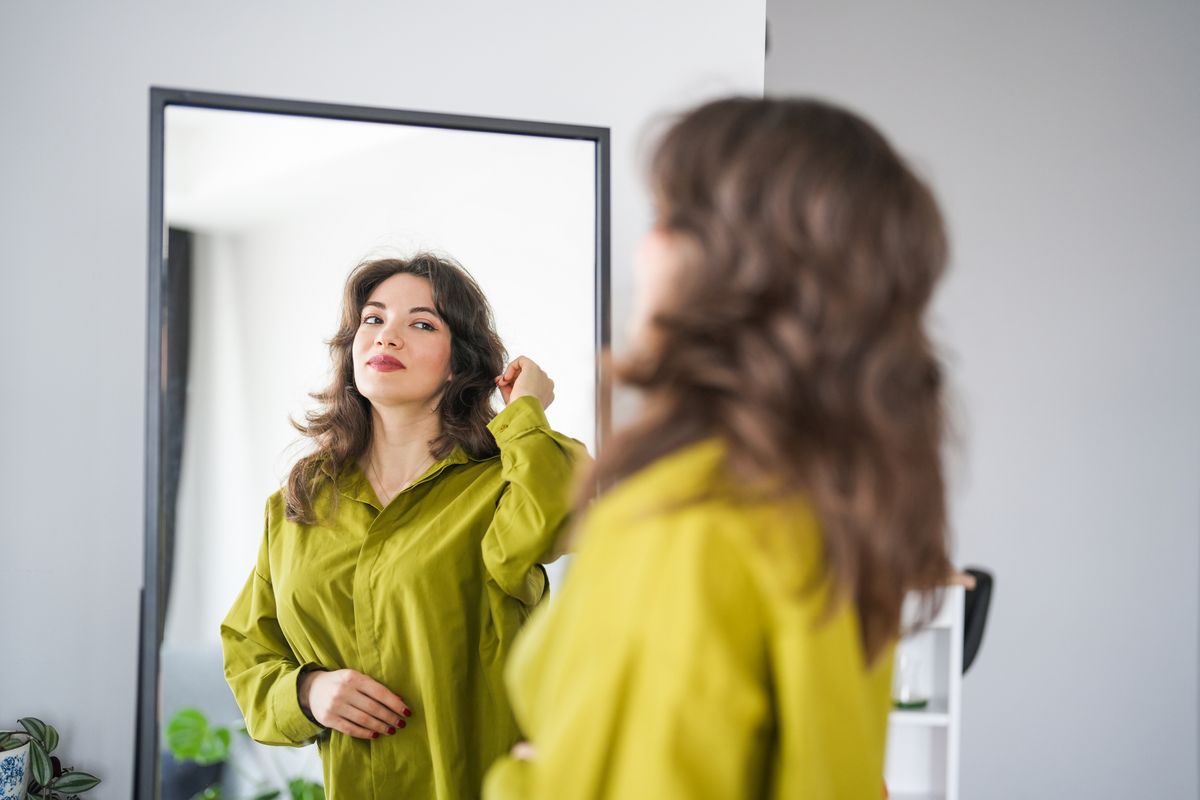 Brunette woman looking at herself in the mirror in the living room of the house