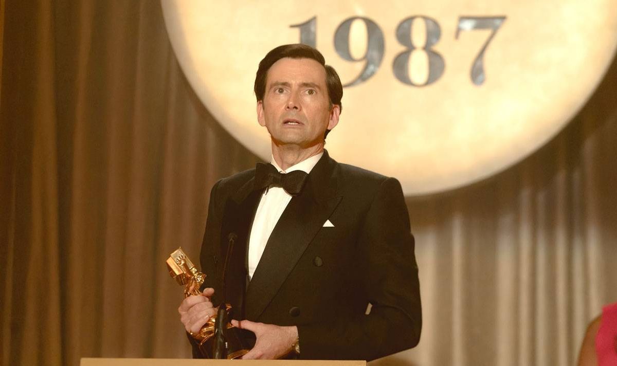 A man in a tuxedo holds an award on a podium