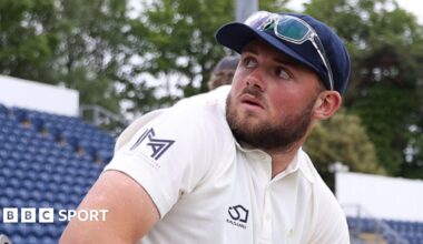 Tom Norton seated on the boundary with glasses on top of cap looks over his shoulder towards the stands at Sophia Gardens