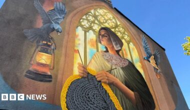 A colourful, large-scale wall painting showing a woman dressed in modest 19th Century clothing while knitting a woollen jumper. She is depicted standing in front of an arched church window through which light streams. To the left, a black bird carries a lamp. Another bird flies to the right.