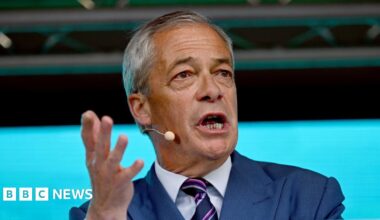 Nigel Farage stood at a lectern with one hand gesturing to his left.