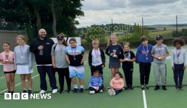 Young members of Mexborough Tennis Club pose for a photograph on a tennis court with an adult