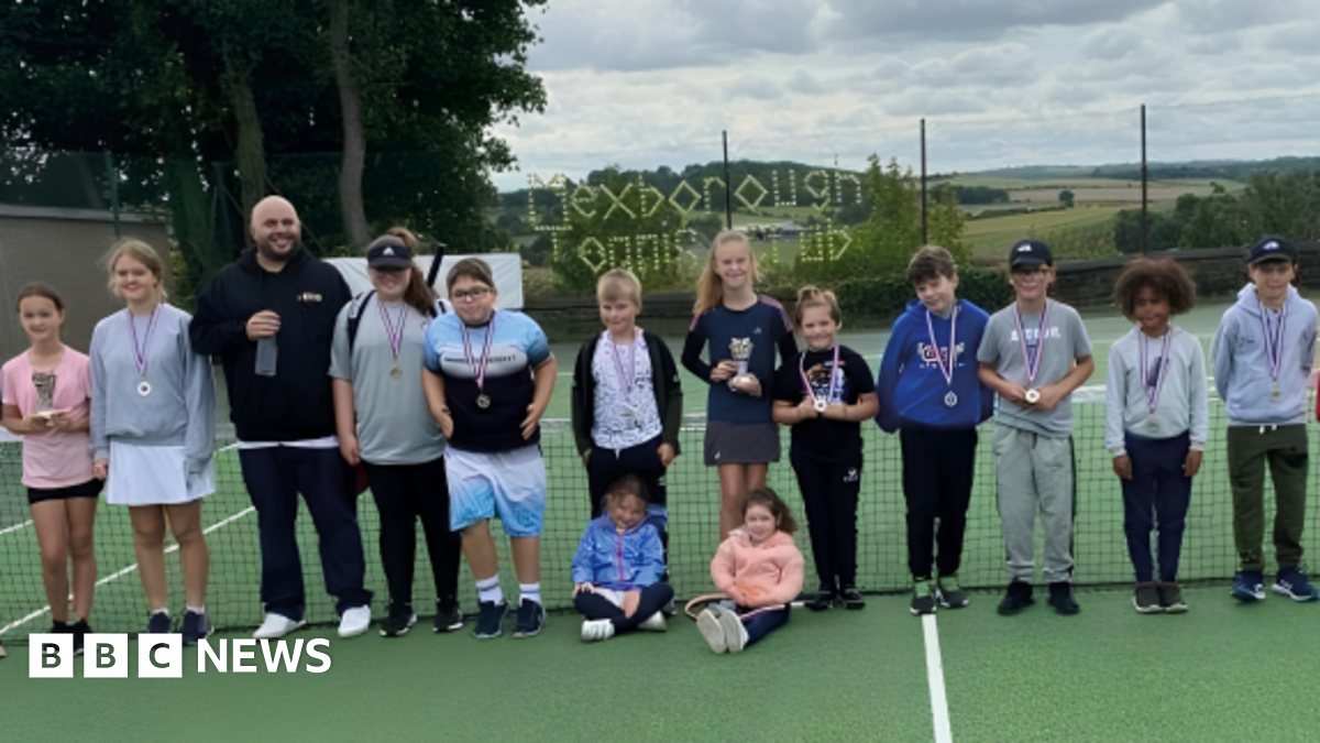 Young members of Mexborough Tennis Club pose for a photograph on a tennis court with an adult