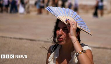 A woman shades her head with a fan in front of Jeronimos Monastery in Belem, Portugal