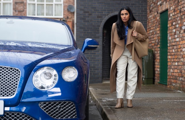 Alya Nazir looking suspicious as she walks towards a blue car in Coronation Street.