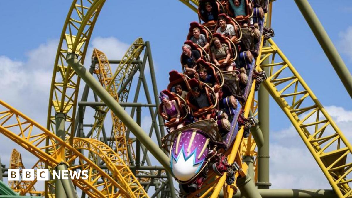 People in a purple rollercoaster race down a yellow track. There are loops and twists on the track behind them.