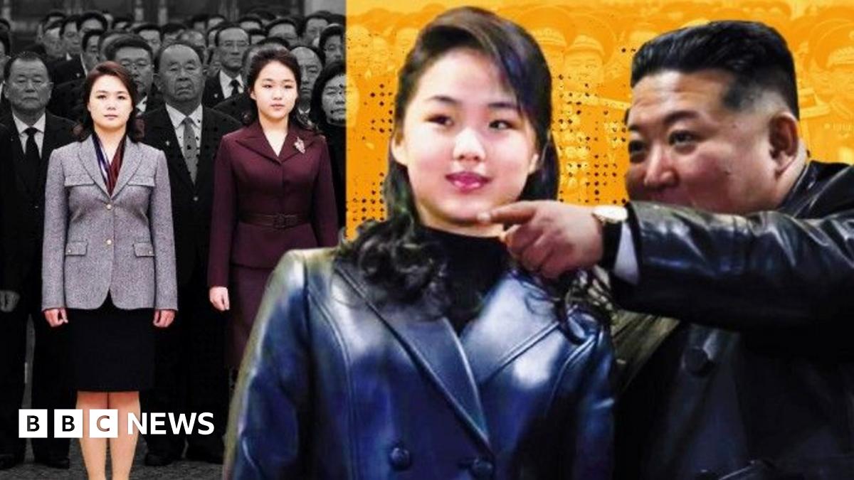 With her long hair tied back, in black trousers and a white padded jacket, Kim Ju Ae walks hand-in-hand with Kim Jong Un, in a brown jacket and black trousers. They are looking towards each other. Towering above them, with several men standing next to it, and hills in the background, an intercontinental ballistic missile (ICBM) points upwards, on a caterpillar-track transporter.