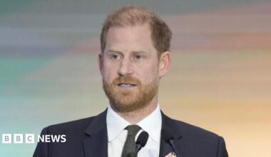 Prince Harry, wearing a dark suit and dark green tie