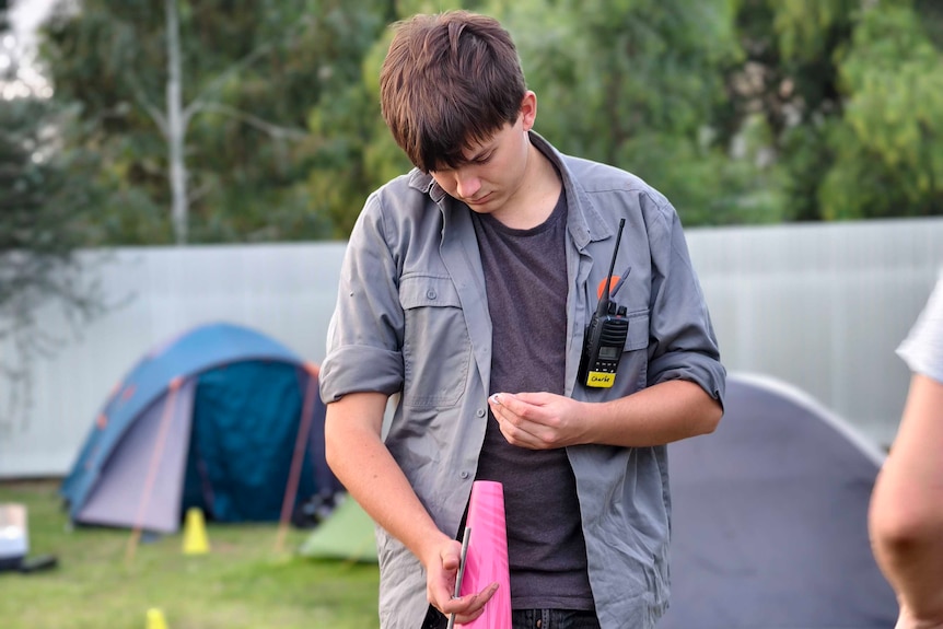 A young man attaching a yellow parachute to a pink rocket nozzle
