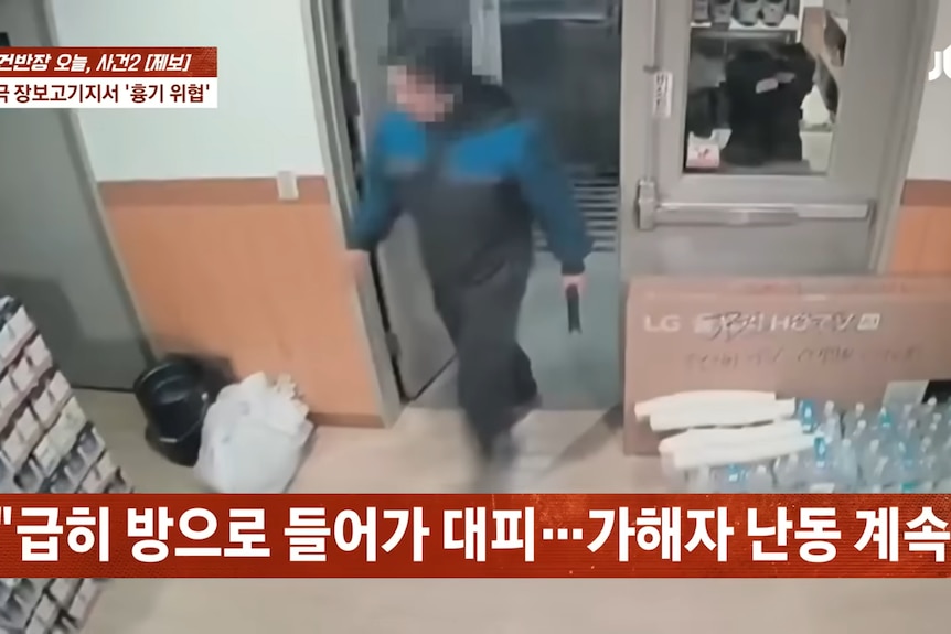 A screenshot of CCTV vision showing a man in a blue and black jacket wielding a knife, with his face blurred.