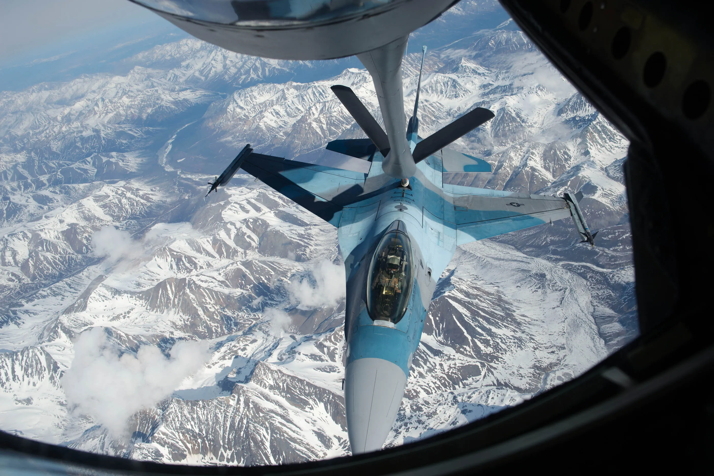 Pictured here, a US fighter jet painted in enemy colors of shades of blue and grey for training purposes is refueled mid-air over the snow mountain rainge in Alaska in May 2017