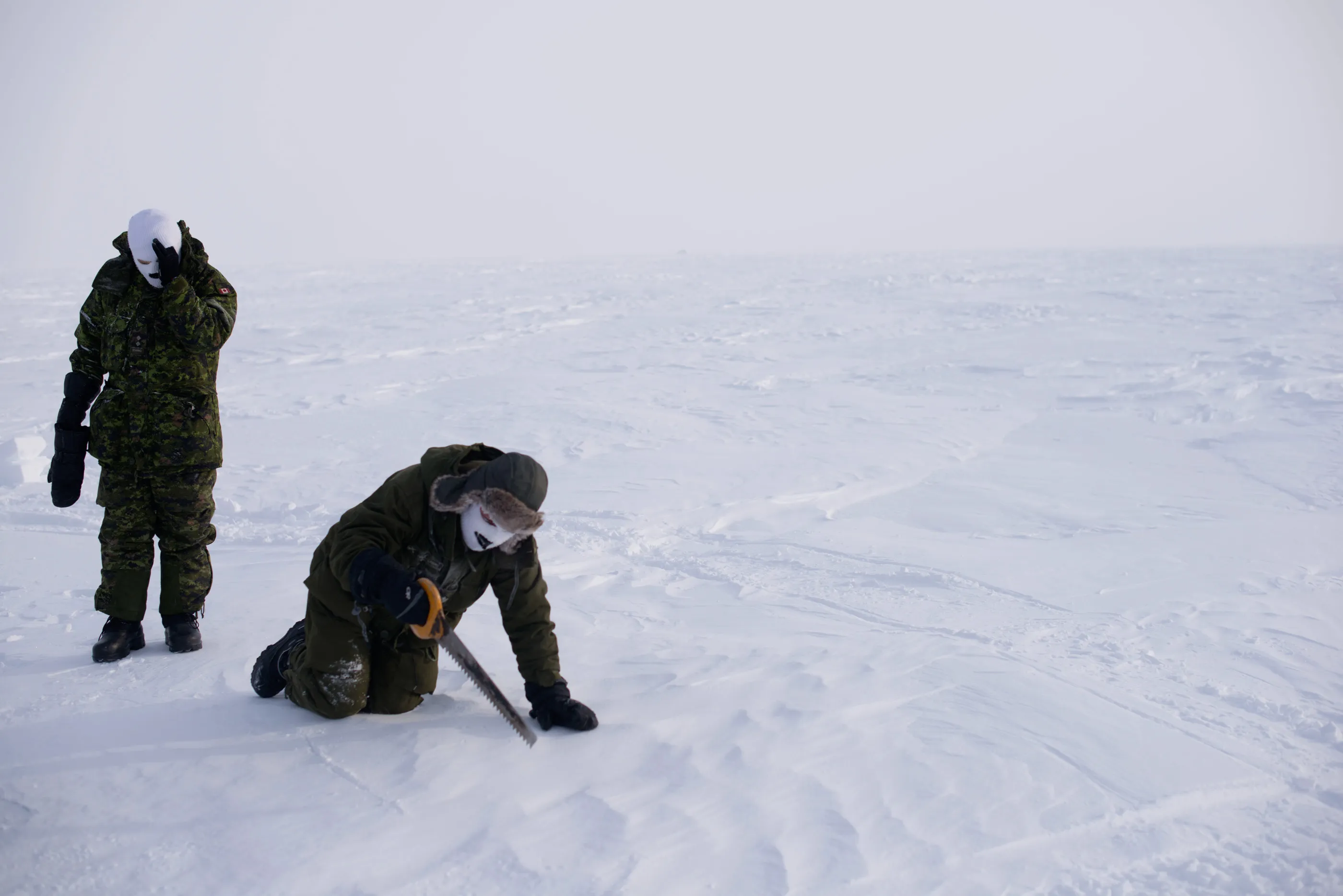 Canadian soldiers saw into the icy snow-covered landscape to test ice for building blocks near Sanirajak in Nunavut. Survival techniques chew up time.