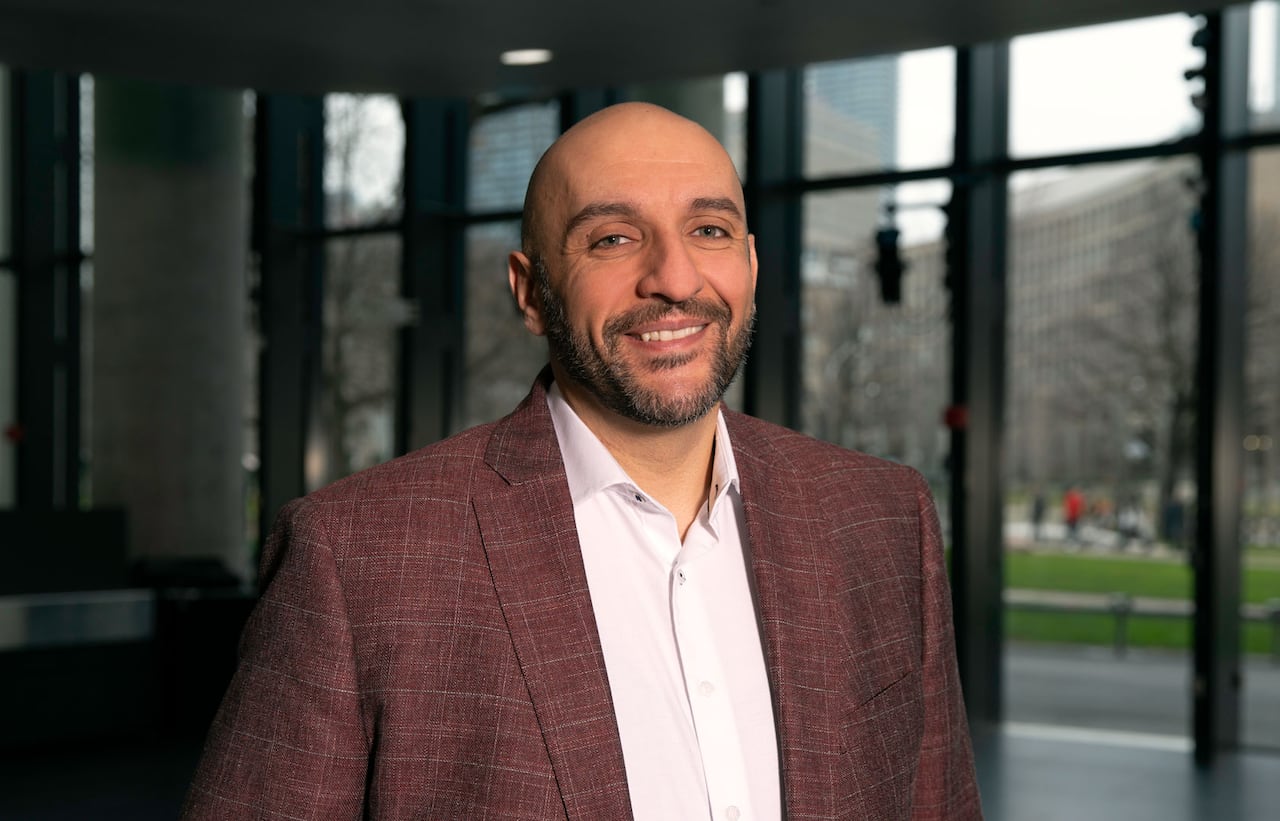 A man in a suit jacket and button-down shirt stands in the lobby of a building.