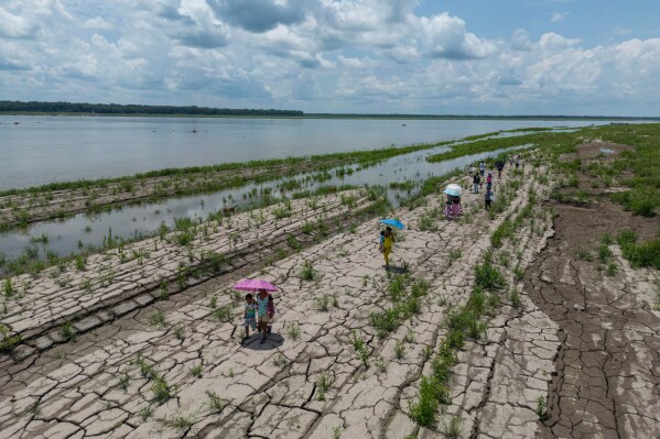 People walk through a part of the Amazon River that shows signs of drought in Santa Sofia, on the outskirts of Leticia, Colombia, Oct. 20, 2024. (AP Photo/Ivan Valencia, File)