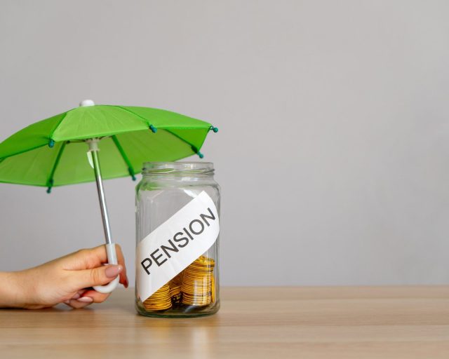 Bank of coins with the inscription Pension and green umbrella. Retirement Insurance concept. Financial support and regular payments to people after retirement. Business and finance