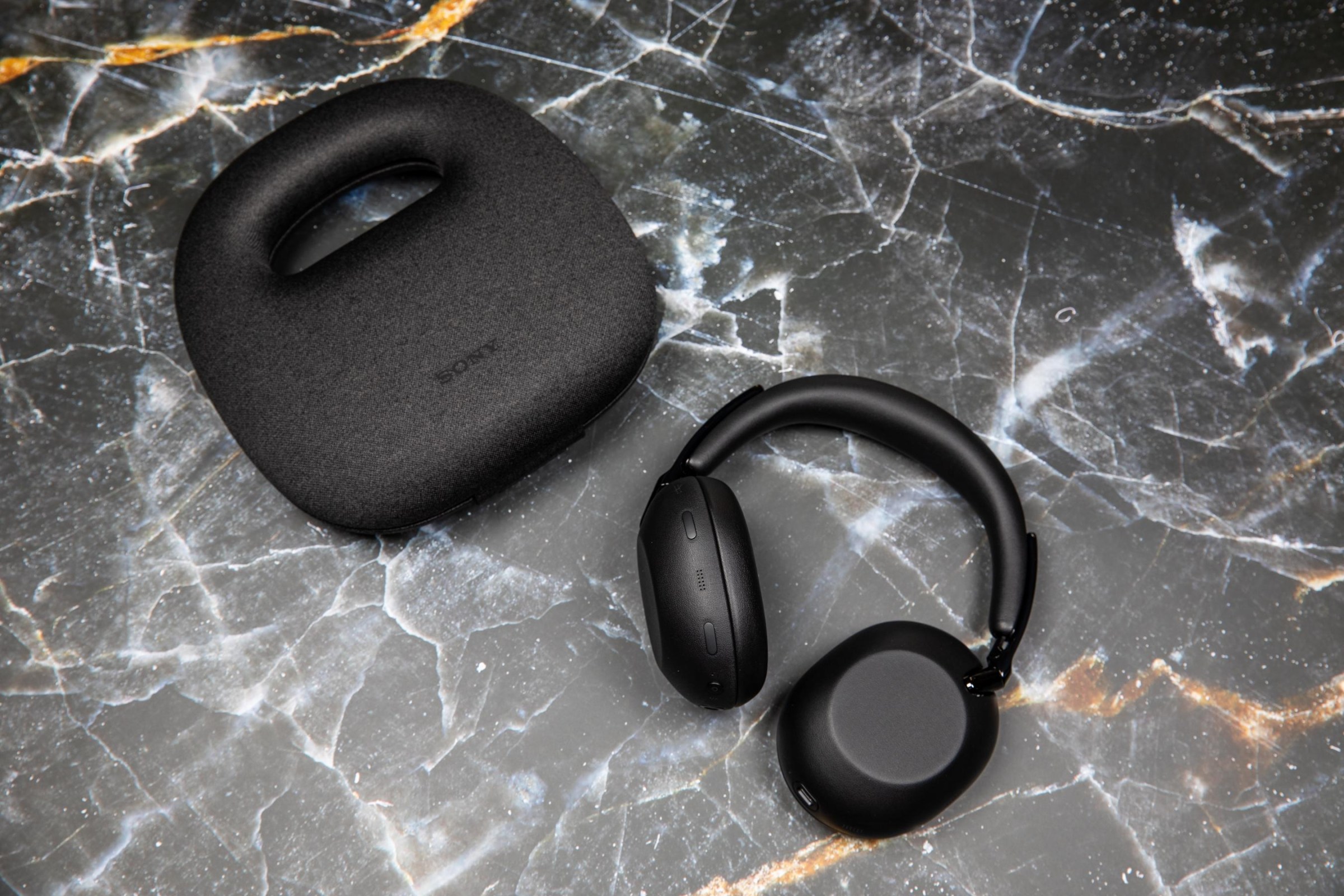 The Sony 1000X The Collexion headphones next to their carrying case on a marble surface.