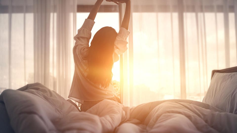 Happy woman stretching in bed after waking up. Happy young girl greets good day.
