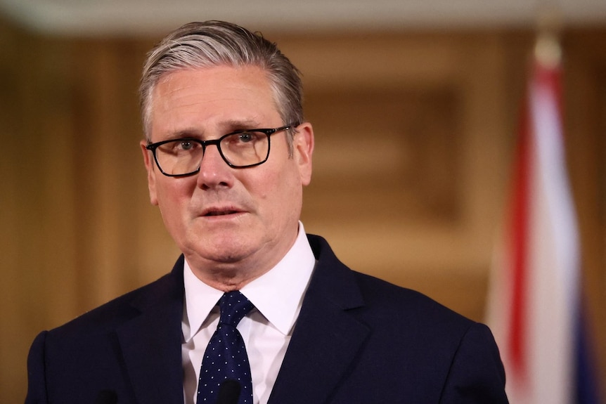 A man in a suit looking on with a neutral expression.