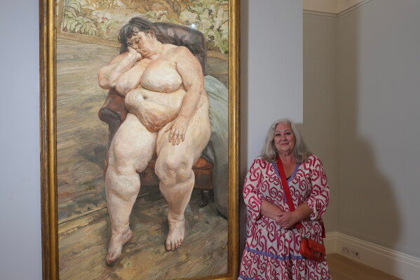 Sue Tilley, a model for British painter Lucian Freud, poses in front of Freud's painting of her, titled "Sleeping by the Lion Carpet" during an interview in Sotheby's auction house in London, Thursday, May 28, 2026. (AP Photo/Kin Cheung)