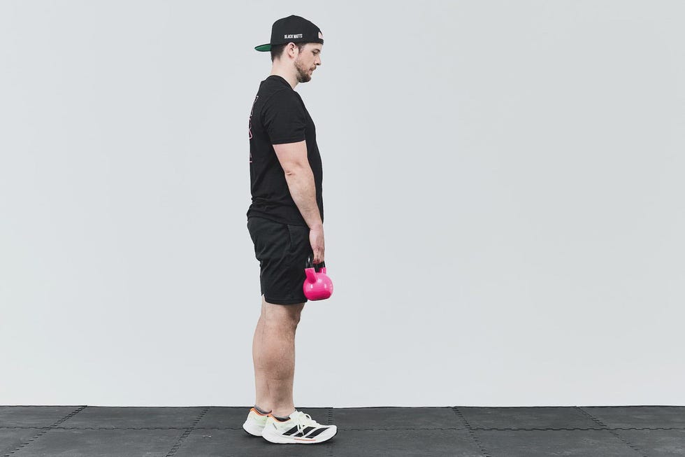 Individual standing sideways holding a pink kettlebell in workout attire.