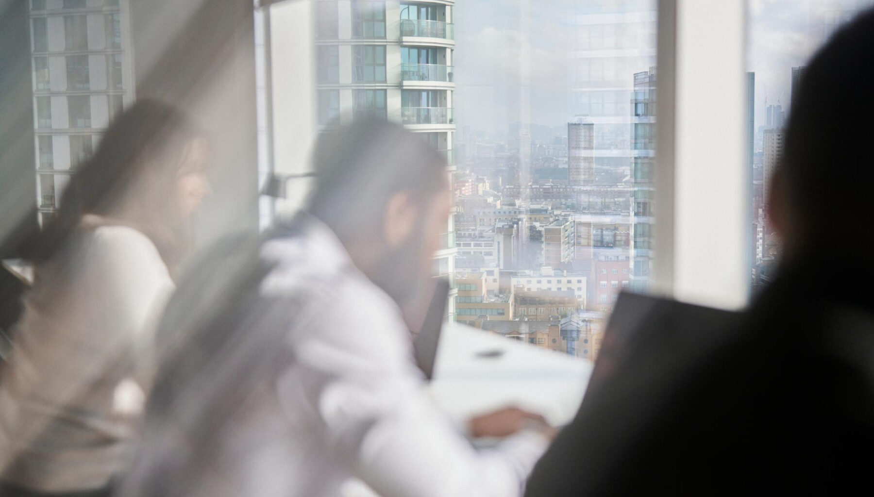 Blurry image of three people with a laptop in a modern office, city view outside window