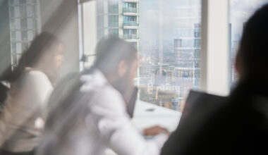 Blurry image of three people with a laptop in a modern office, city view outside window