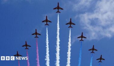 Nine red arrows are seen in formation, leaving trails of red, white and blue vapour, during a display in the sky