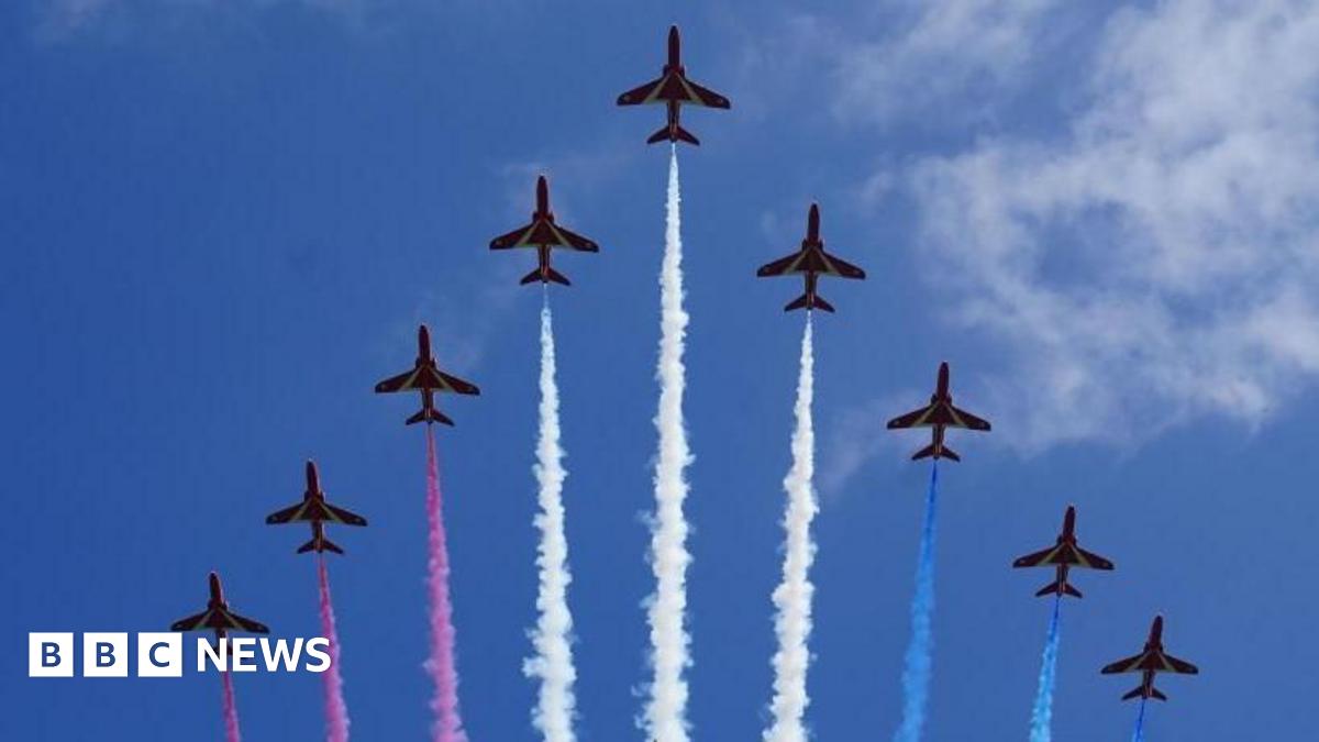Nine red arrows are seen in formation, leaving trails of red, white and blue vapour, during a display in the sky