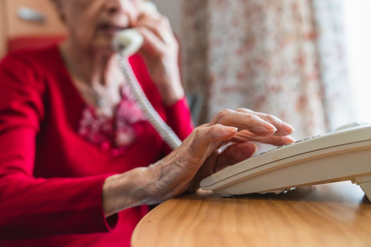 Senior woman dialing a phone number on a landline phone