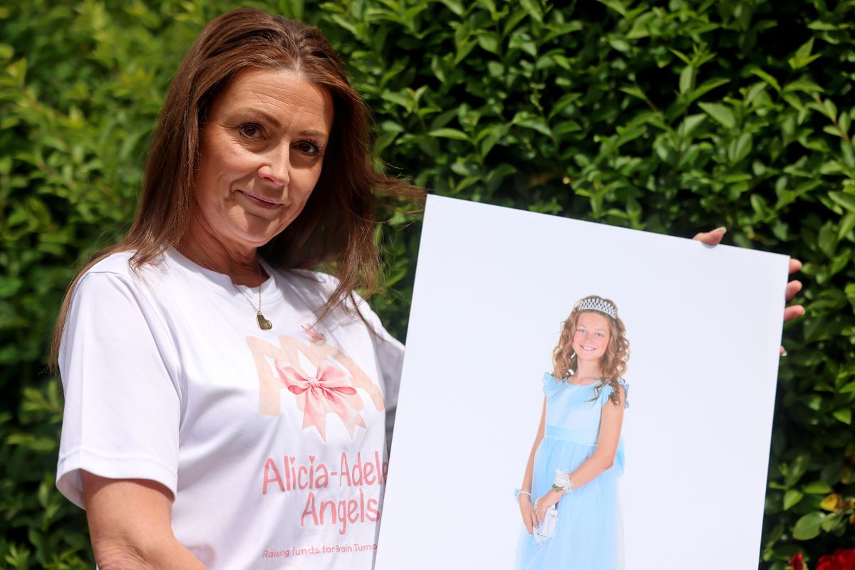 A dark haired woman holding up a picture showing a little girl wearing a blue dress