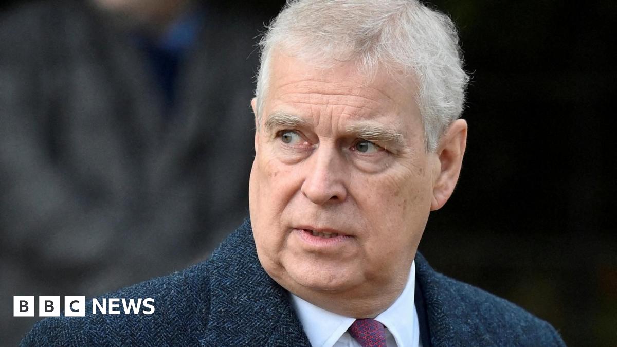 Headshot of Andrew who looks off to the side with his mouth slightly open. The background is blurry but it appears there's a person walking behind him. Taken in December 2022