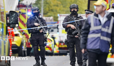 Armed police at the scene, with police vehicles in the background.