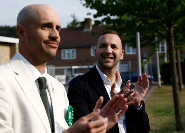 Two men, one in a white suit, stand outside an election counting centre in London.