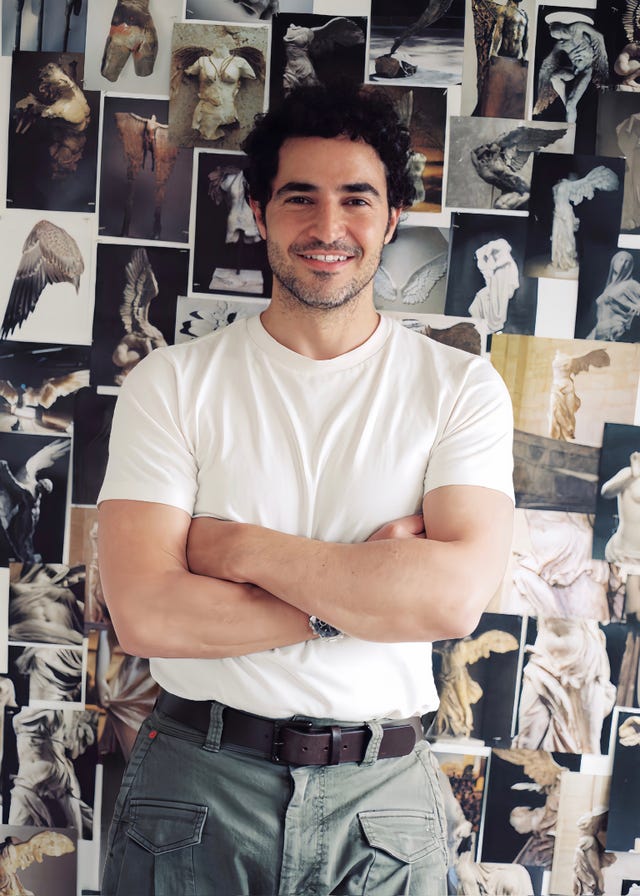 Person posing in front of a wall filled with art photographs