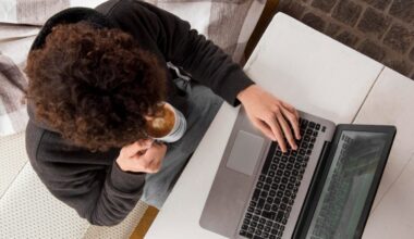 A photo from above showing a person holding a cup of coffee while typing on a laptop